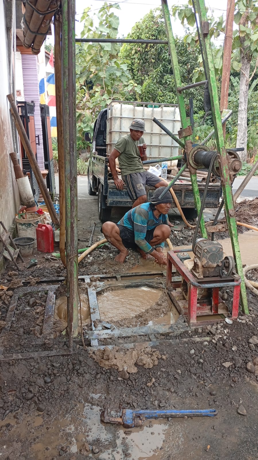 Proses pengeboran sumur bor di area rumah, mesin bor dan pekerja terlihat